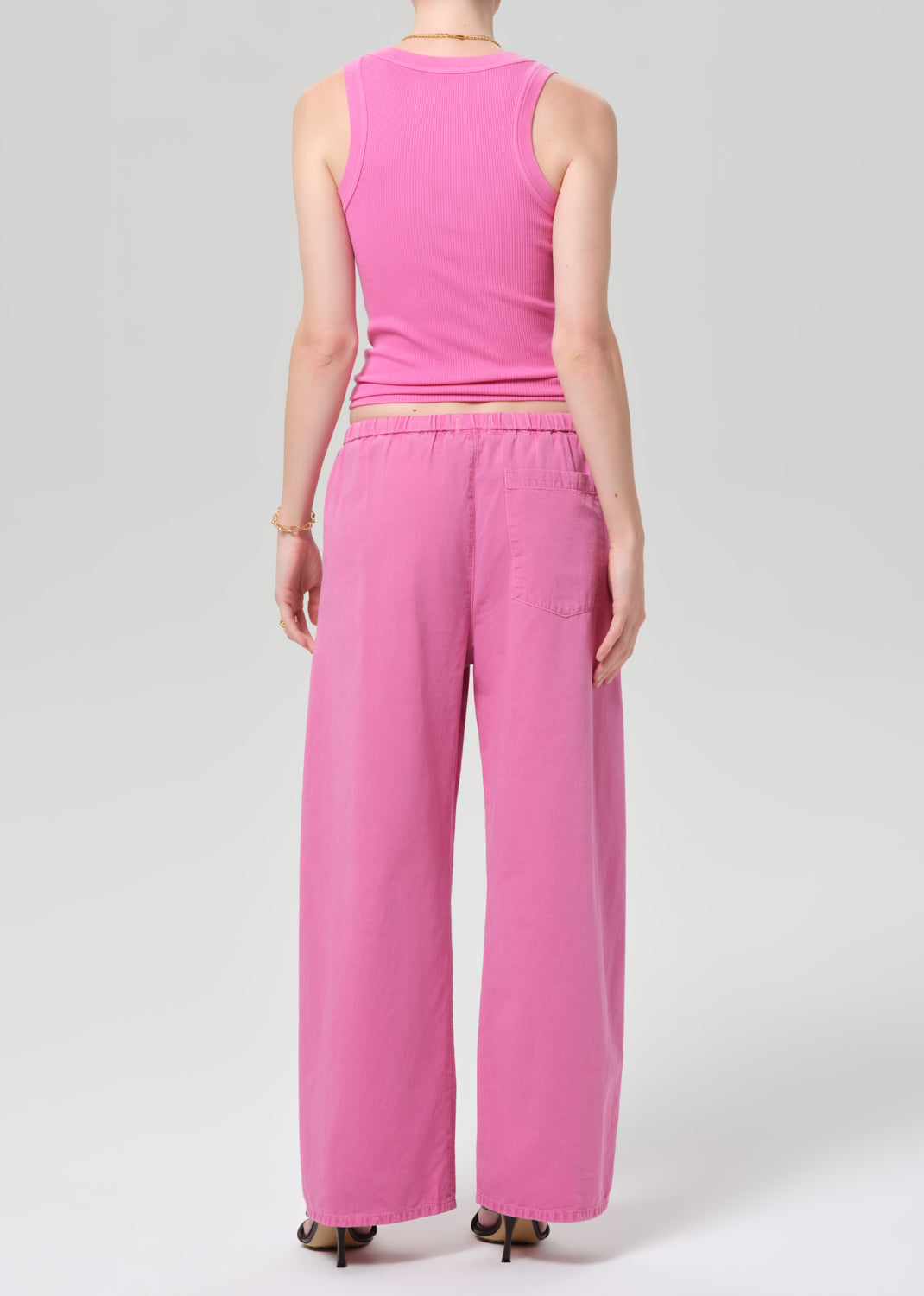 Person wearing a pink sleeveless top and wide-leg pants on a plain background