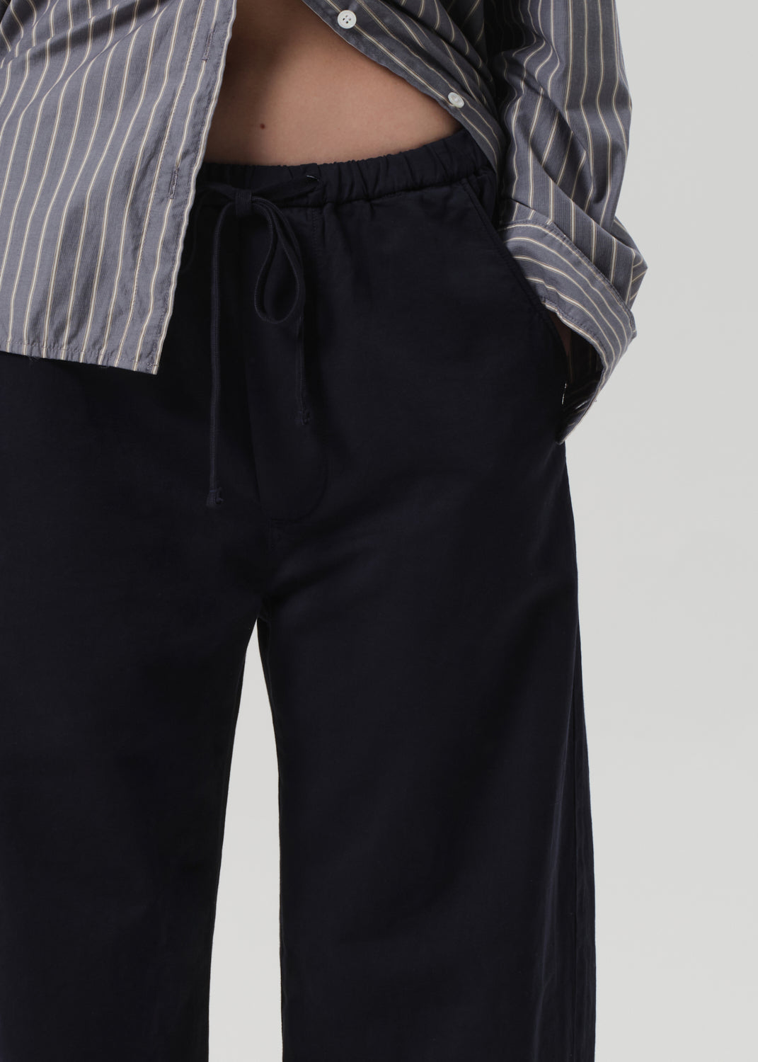 Person wearing a striped shirt and navy pants on a grey background