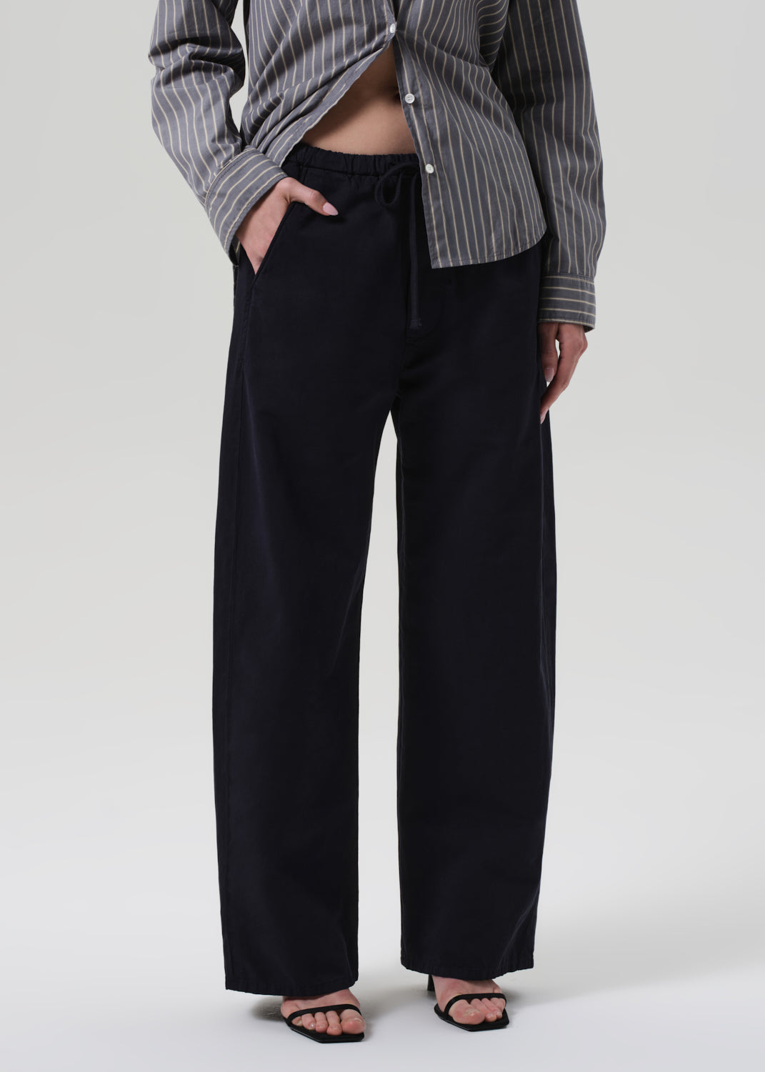 Person wearing a striped shirt and navy pants on a grey background