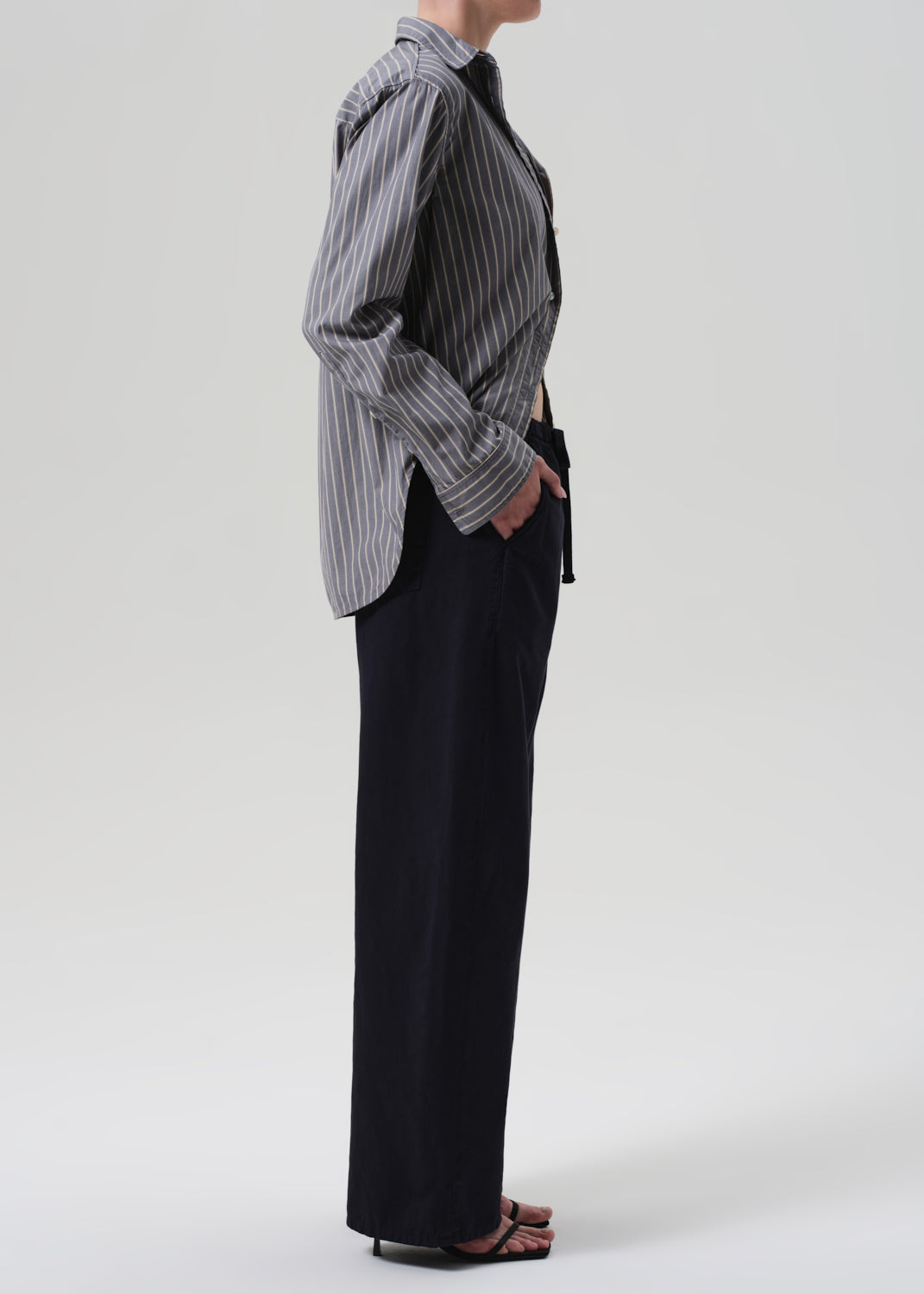 Person wearing a striped shirt and navy pants on a grey background