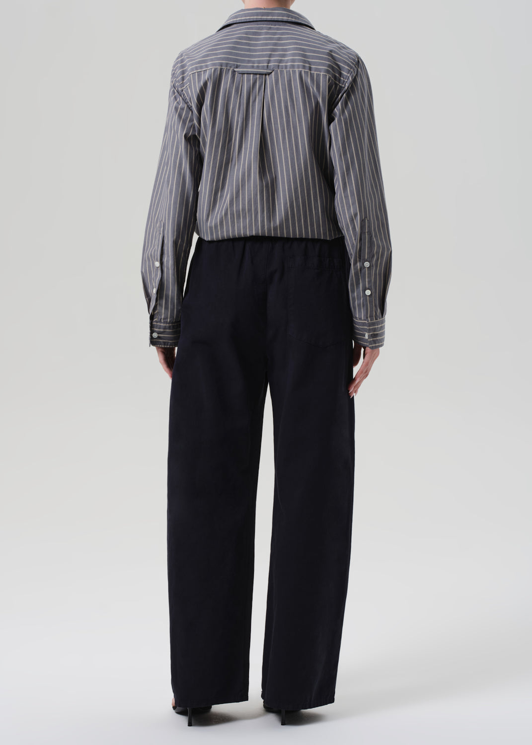 Person wearing a striped shirt and navy pants on a grey background