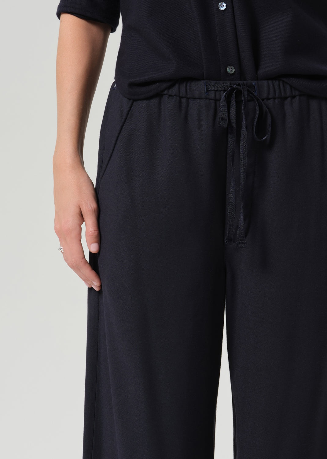 Close-up of a person wearing dark navy wide-leg trousers with an elastic drawstring waistband, paired with a matching dark top against a grey background.