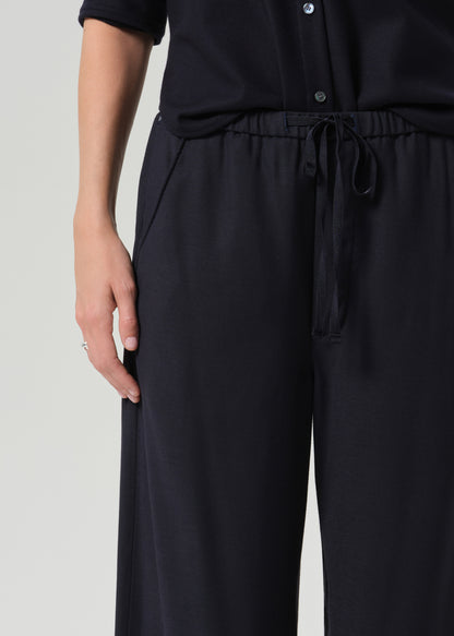 Close-up of a person wearing dark navy wide-leg trousers with an elastic drawstring waistband, paired with a matching dark top against a grey background.