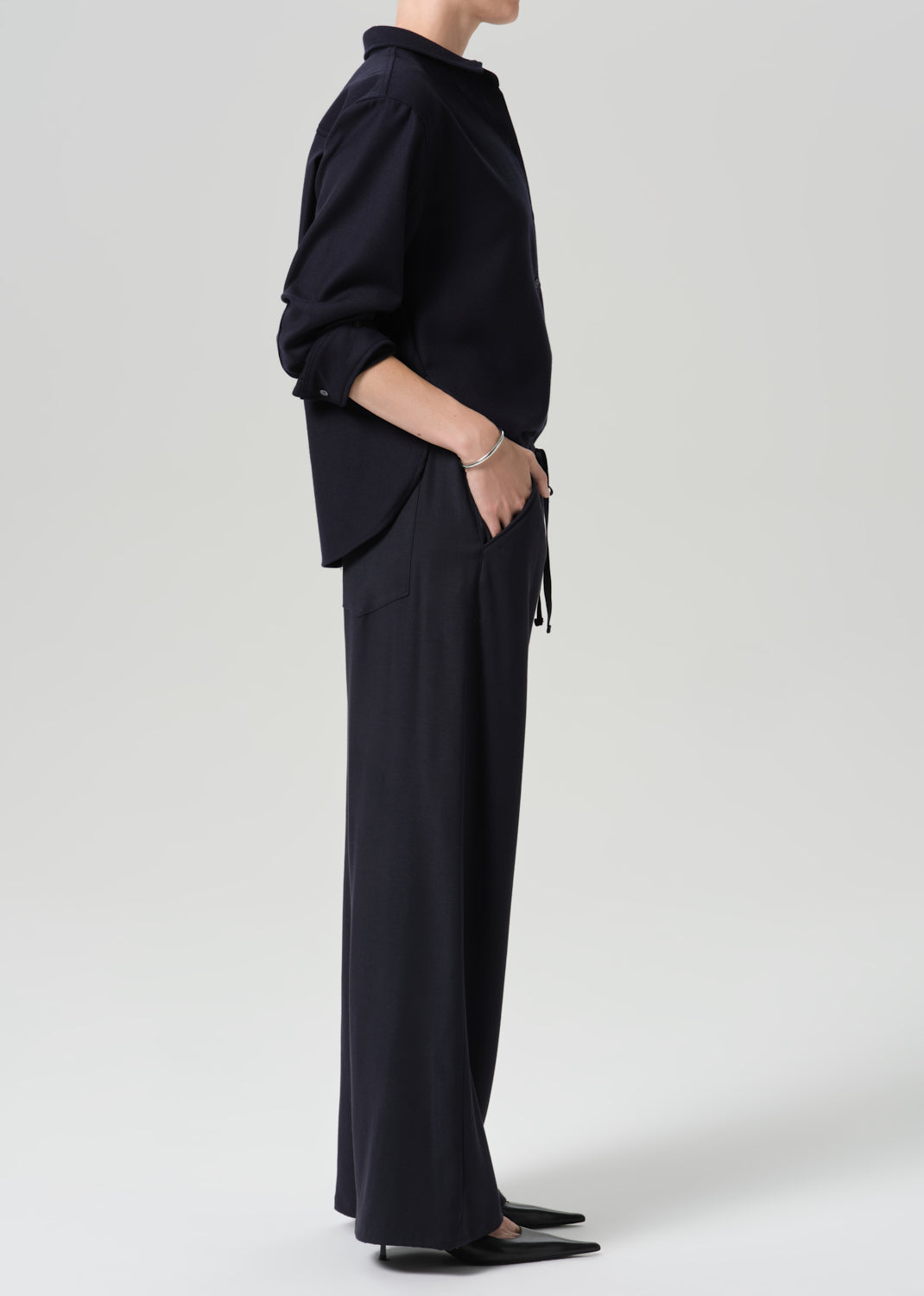 A model shown from the side wearing a dark navy blue long-sleeve top and matching wide-leg trousers against a grey background.