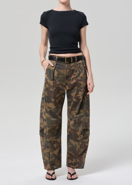 Person wearing camouflage pants and a black top on a plain background