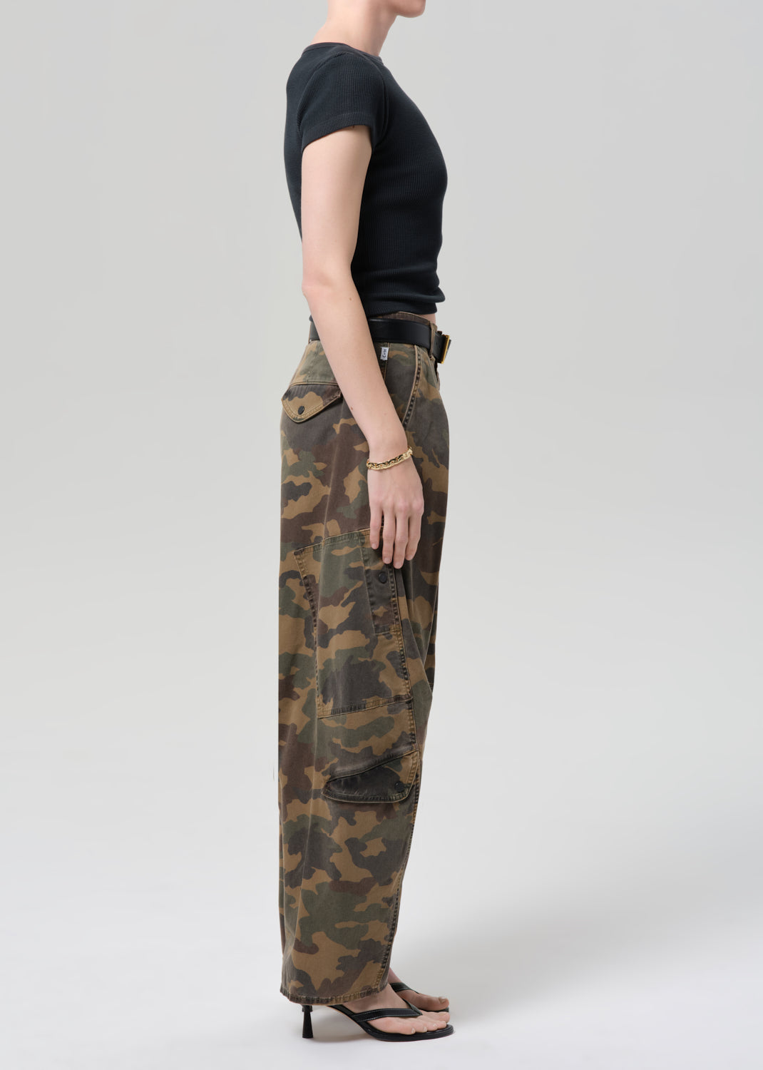 Person wearing camouflage pants and a black top on a plain background