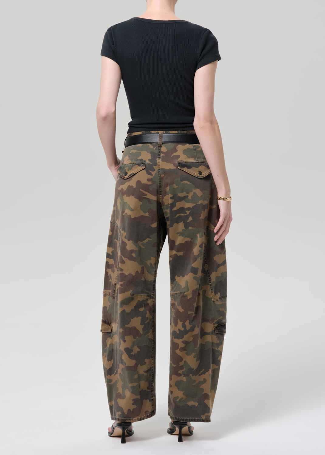 Person wearing camouflage pants and a black top on a plain background