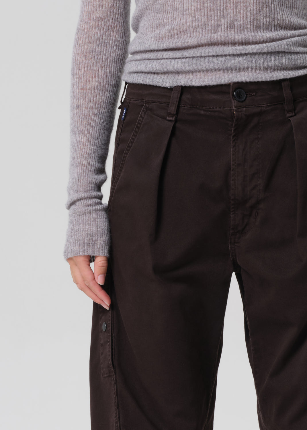 Brown pleated pants worn with a gray sweater on a light gray background
