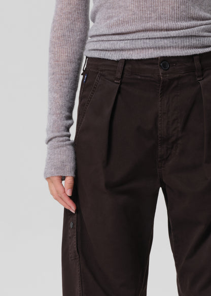 Brown pleated pants worn with a gray sweater on a light gray background