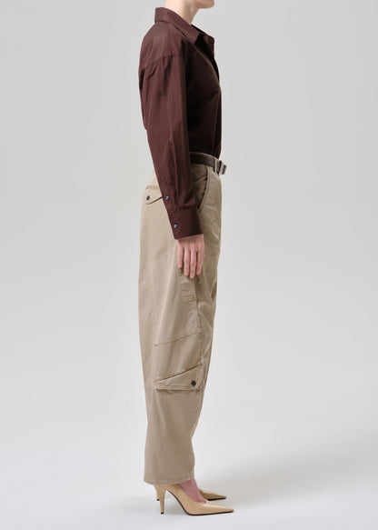 A model shown from the side wearing a dark brown long-sleeve collared shirt tucked into beige cargo pants with a dark belt, paired with beige high-heeled pumps, against a grey background.