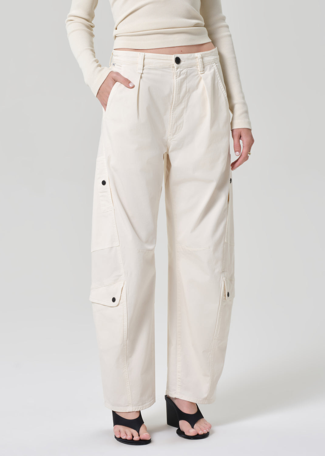 Person wearing a cream long-sleeve top and cream pants on a grey background