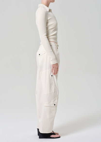 Person wearing a cream long-sleeve top and cream pants on a grey background