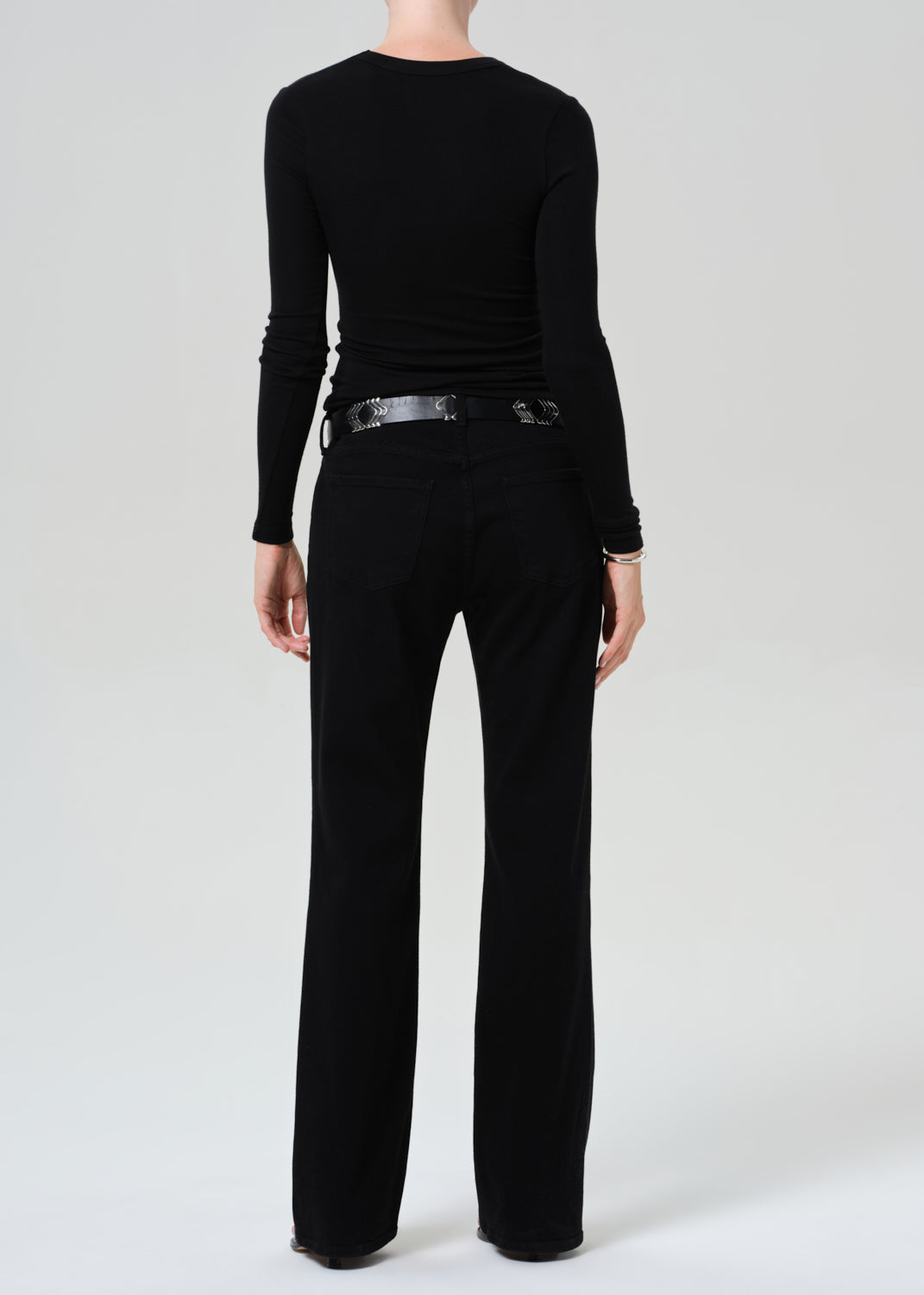 Person wearing a black long-sleeve top and black jean on a plain background