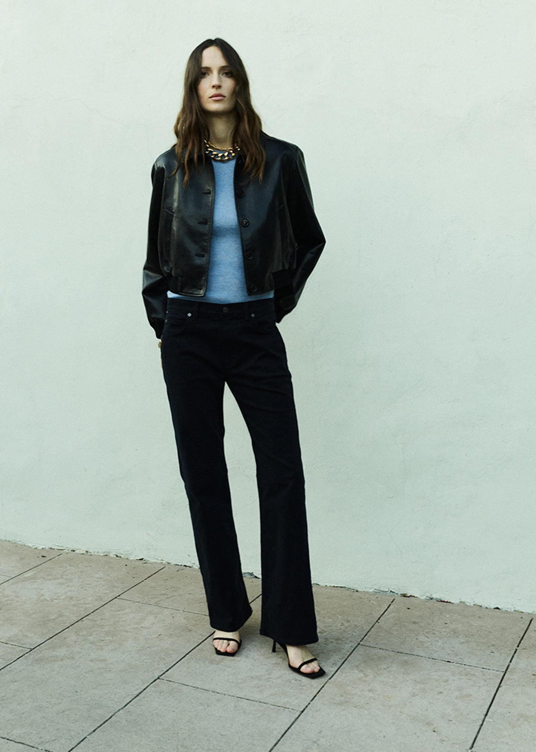 Woman wearing a black leather jacket and navy pants against a light gray background