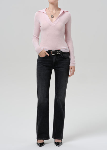 Person wearing a light pink ribbed V-neck sweater with black straight leg jeans on a grey background
