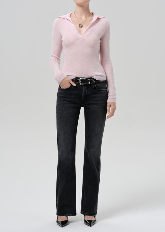 Person wearing a light pink ribbed V-neck sweater with black straight leg jeans on a grey background