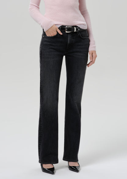 Person wearing a light pink ribbed V-neck sweater with black straight leg jeans on a grey background