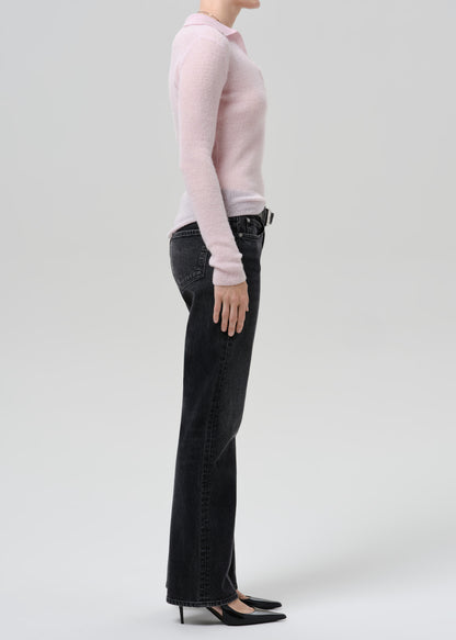 Person wearing a light pink ribbed V-neck sweater with black straight leg jeans viewed from the side on a grey background