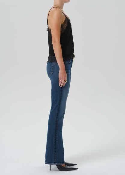 A model shown from the side wearing a black lace-trimmed camisole top, blue flare jeans, and black pointed-toe heels against a grey background.