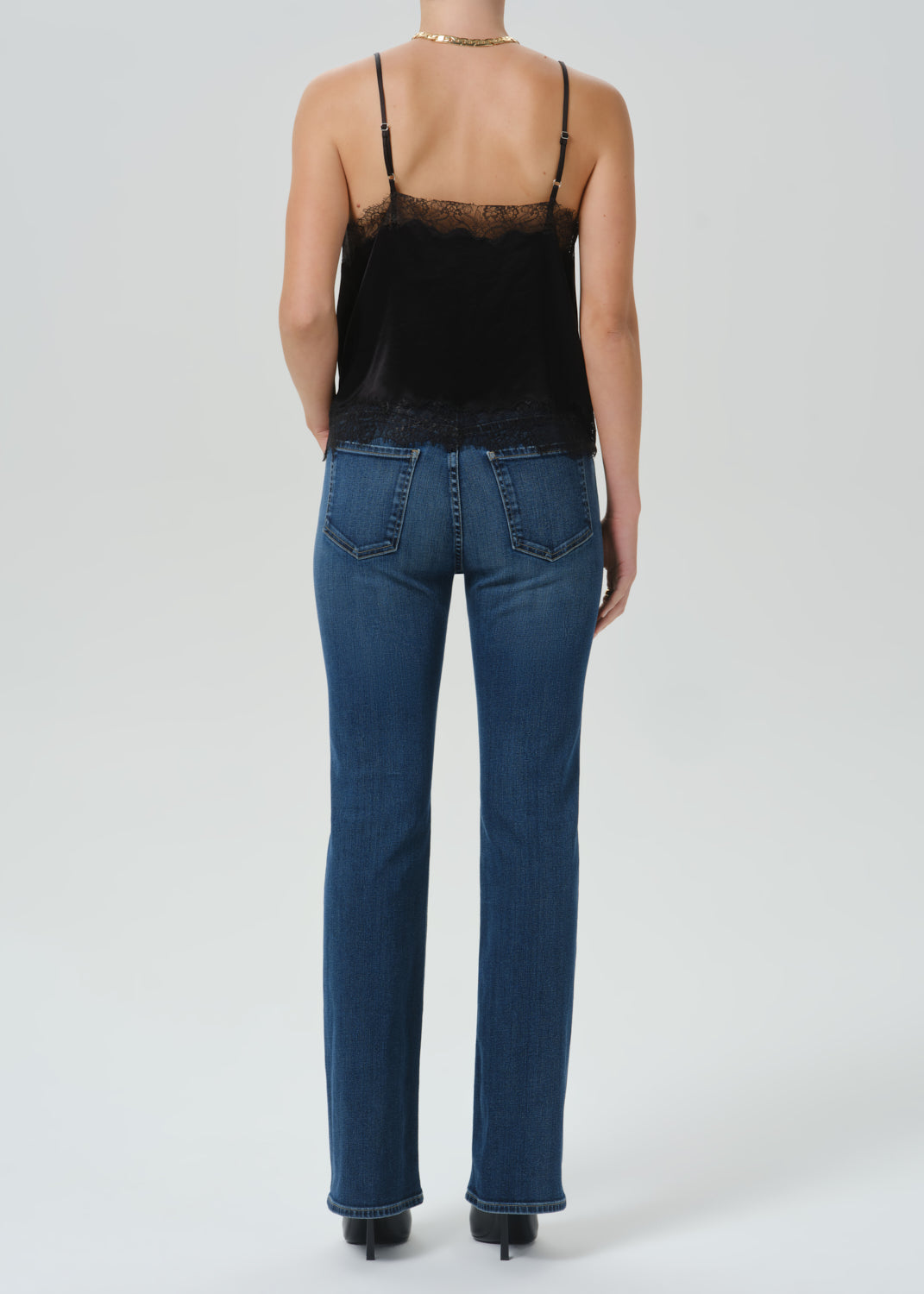 A model shown from the back wearing a black lace-trim camisole top and blue jeans against a grey background.