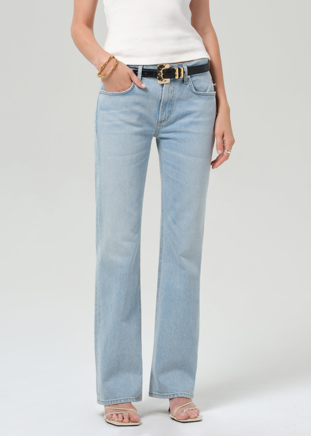 Person wearing light blue jeans and a white top on a plain background