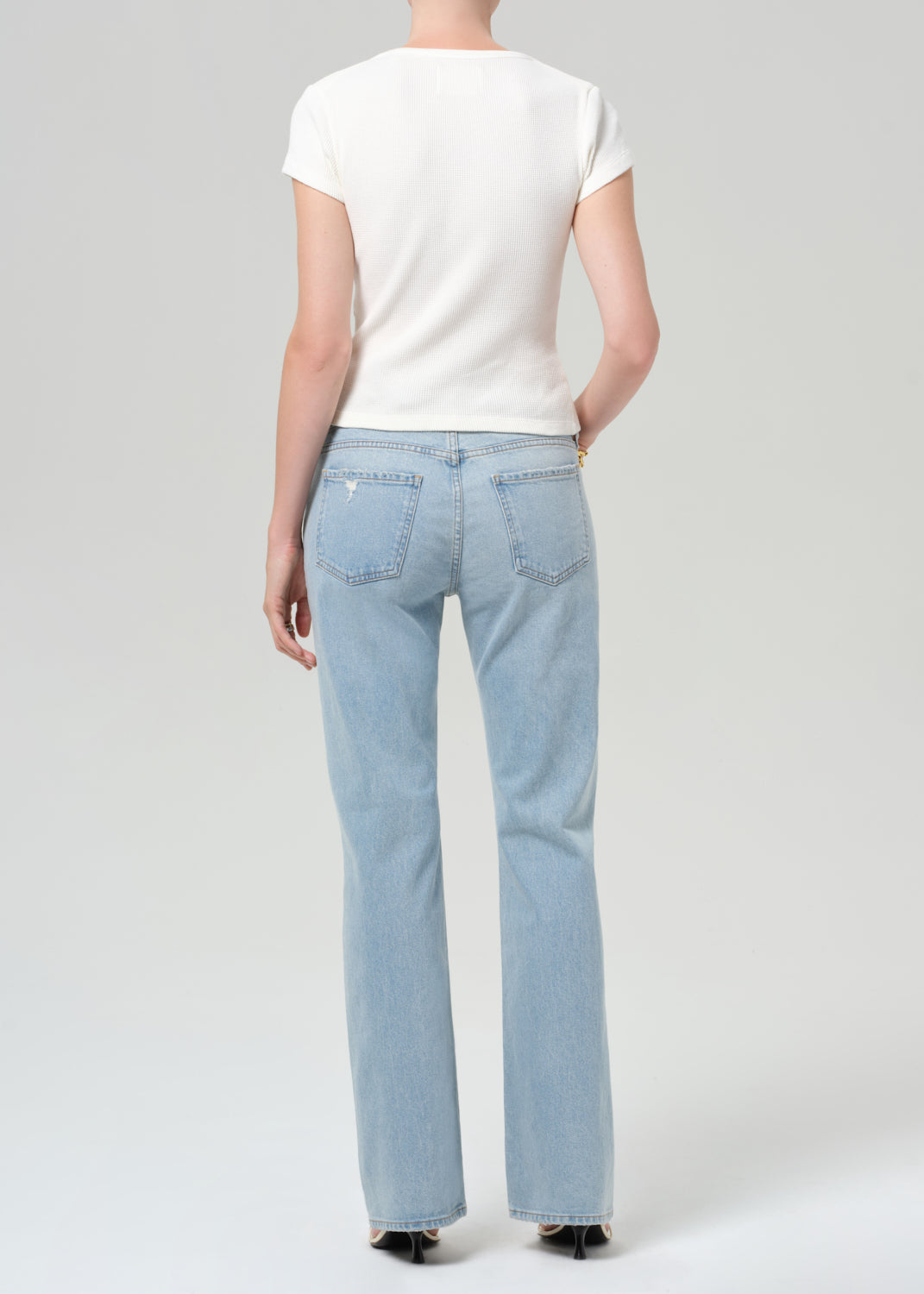 Person wearing light blue jeans and a white top on a plain background