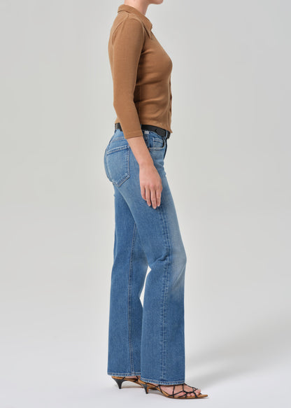 Person wearing a brown top and blue jeans on a light gray background