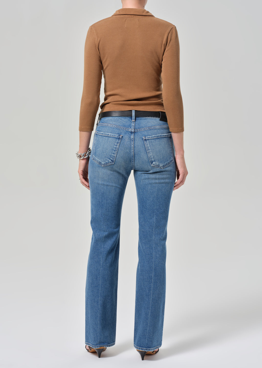 Person wearing blue jeans and a brown top on a plain background