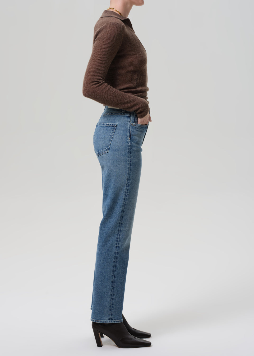 Person wearing blue jeans and a brown sweater on a grey background