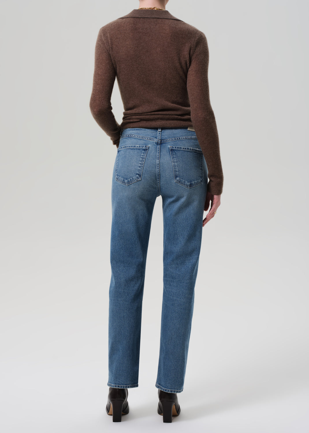 Person wearing blue jeans and a brown sweater on a grey background