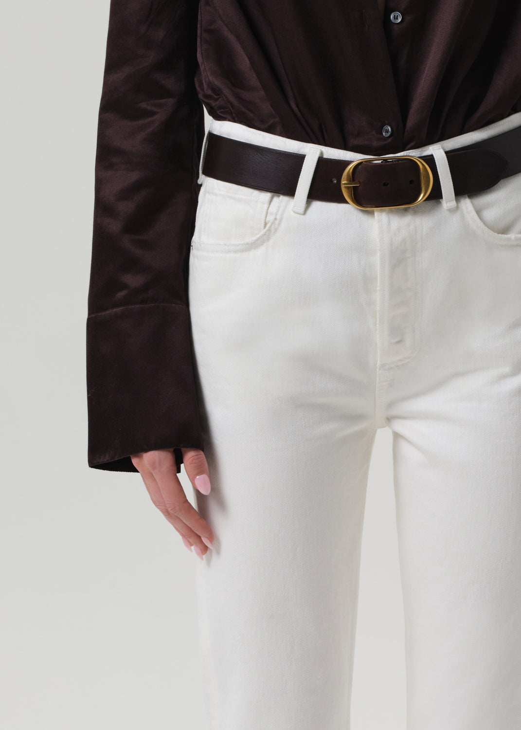 Person wearing a brown shirt and white pants on a plain background