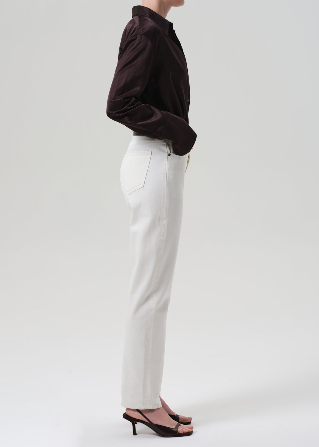 Person wearing a brown shirt and white pants on a plain background
