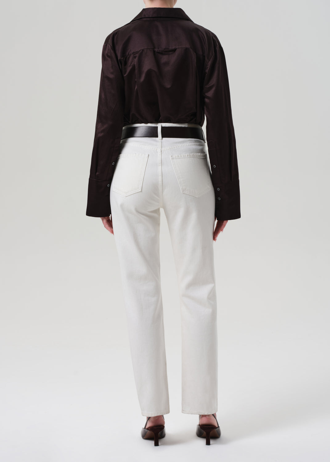 Person wearing a brown shirt and white pants on a plain background