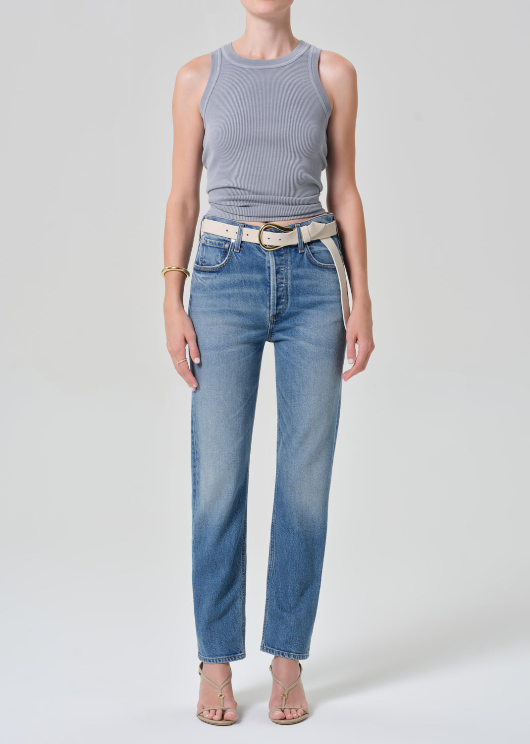 Person wearing a gray tank top and blue jeans with a grey background