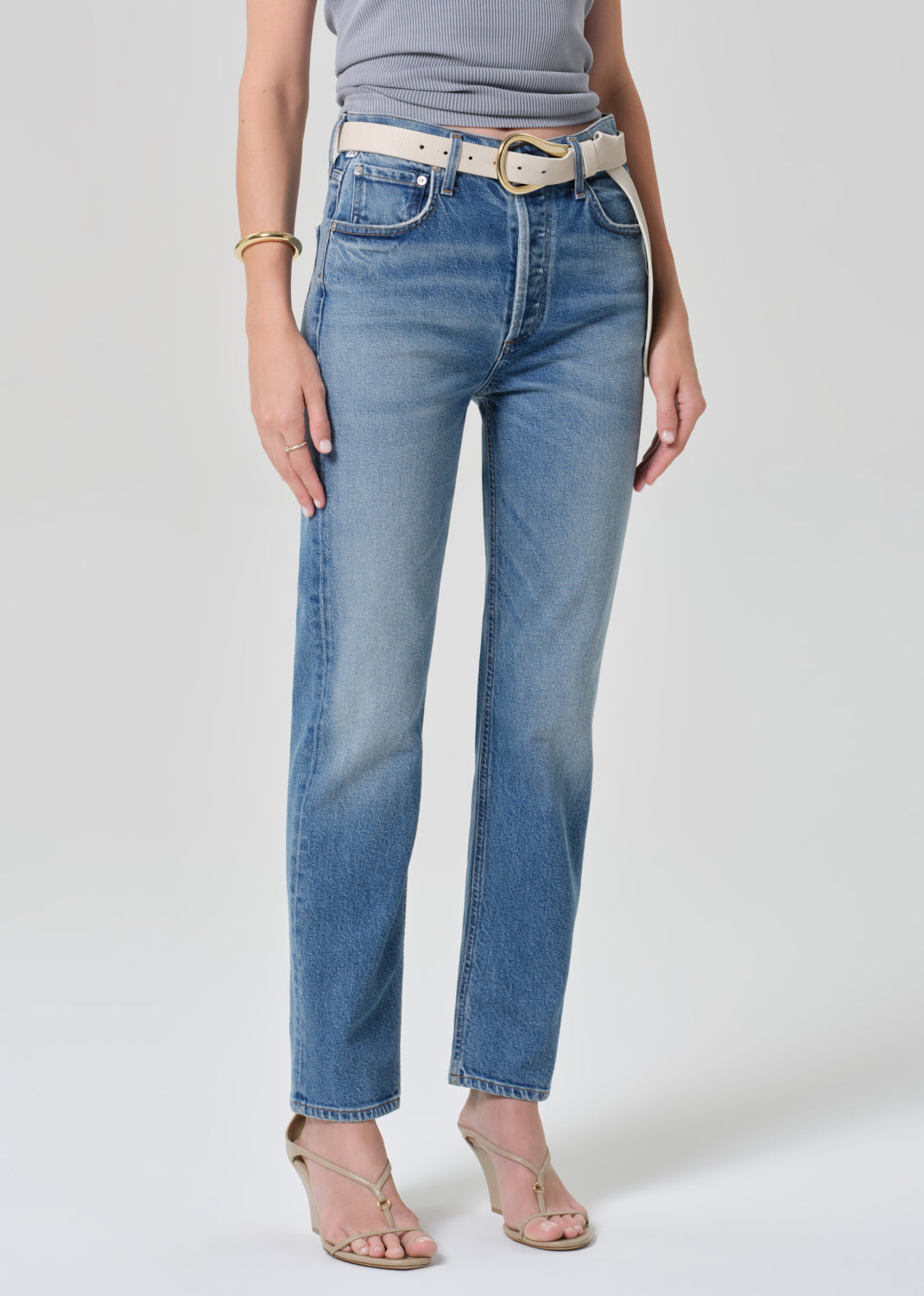 Person wearing light blue jeans with a white belt on a plain background