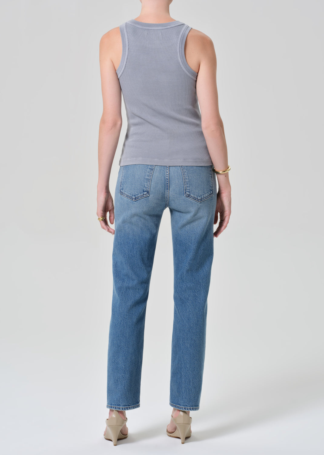 Person wearing a gray tank top and blue jeans on a grey background