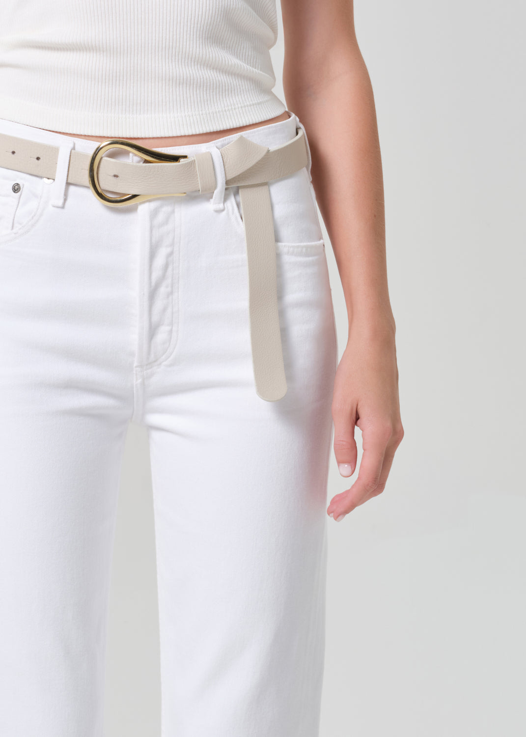 Person wearing a white tank top and white jeans on a plain background