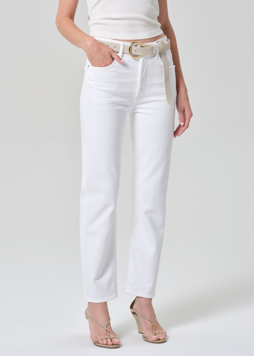 Person wearing a white tank top and white jeans on a plain background