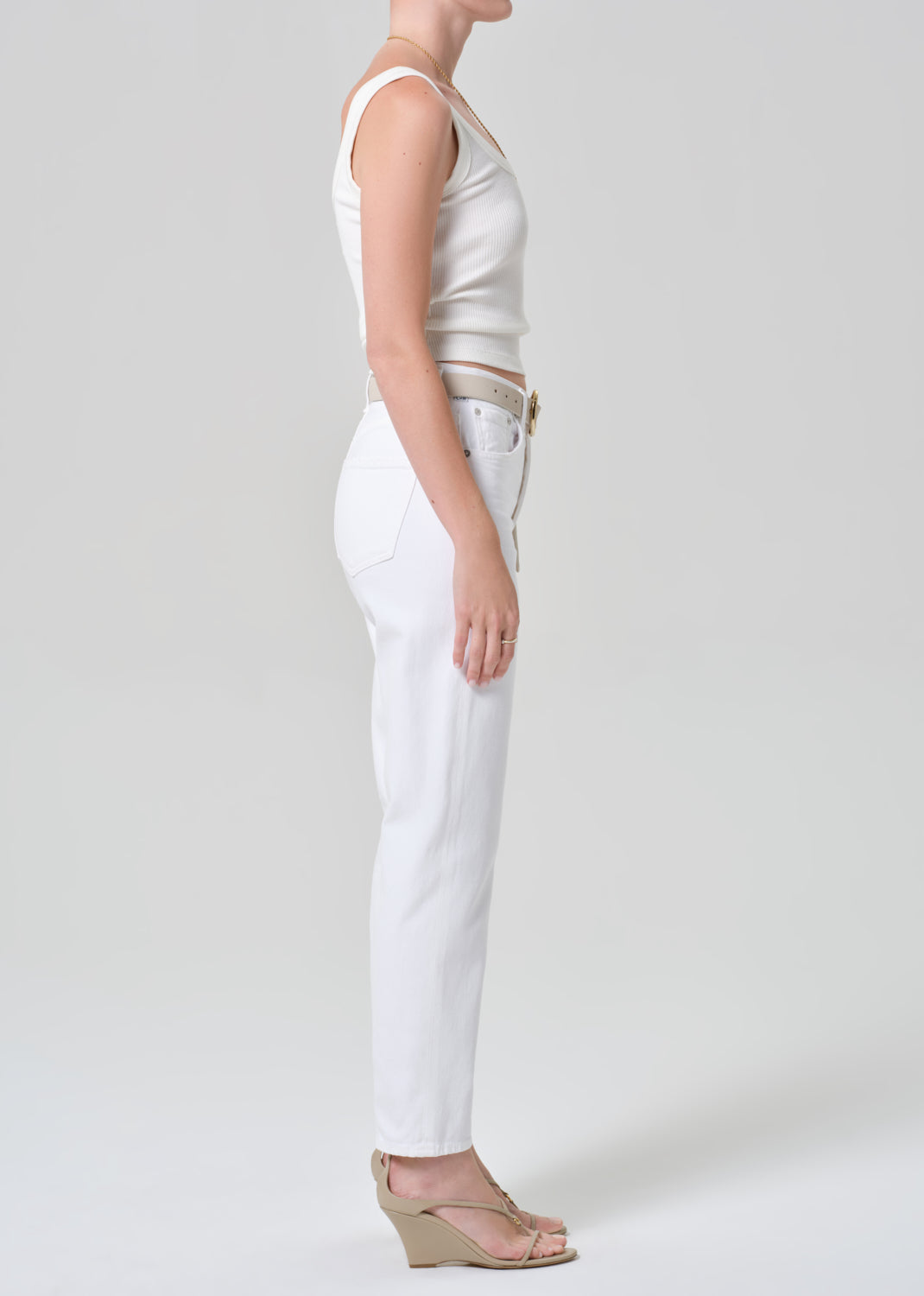 Person wearing a white tank top and white jeans on a plain background