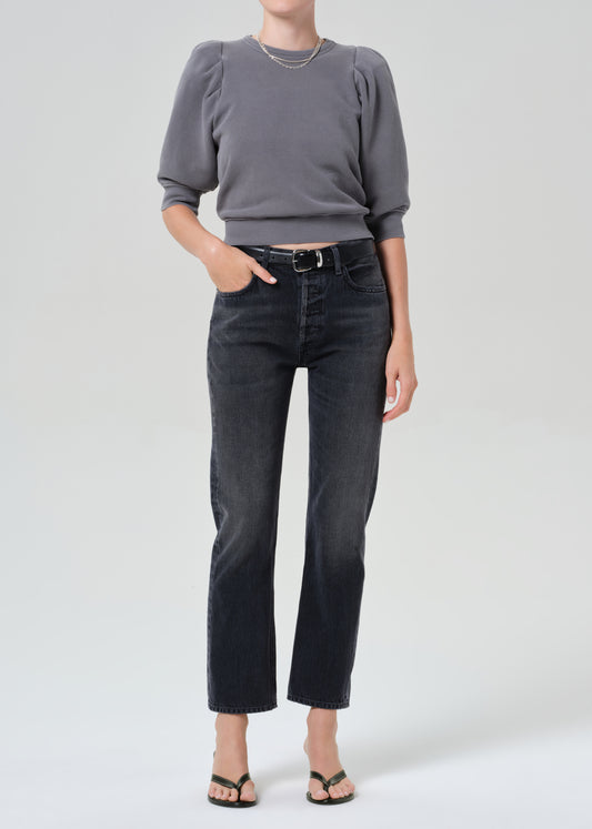 Person wearing a gray sweater and black jeans on a grey background