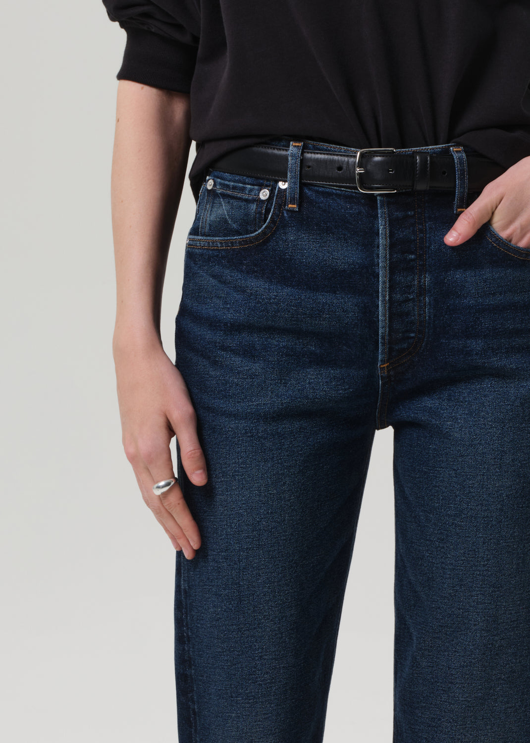 Person wearing a black sweater and dark blue jeans on a grey background