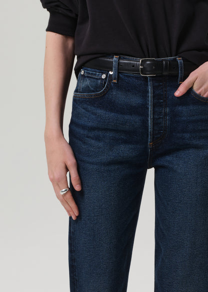 Person wearing a black sweater and dark blue jeans on a grey background