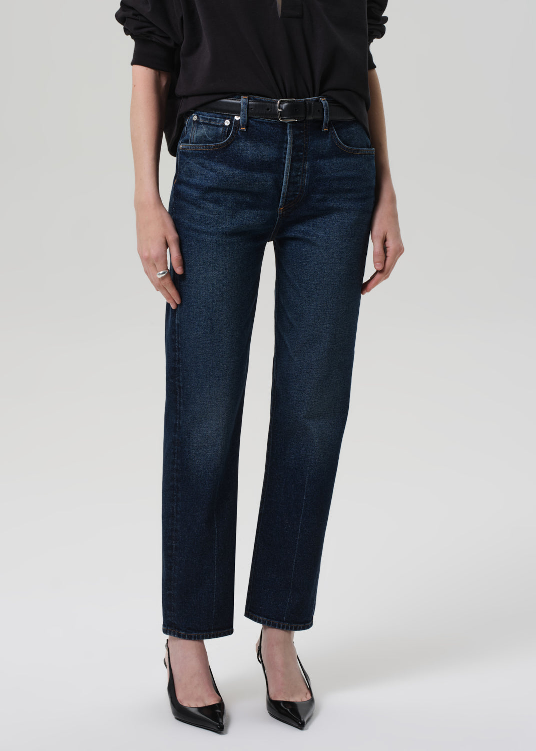 Person wearing a black sweater and dark blue jeans on a grey background