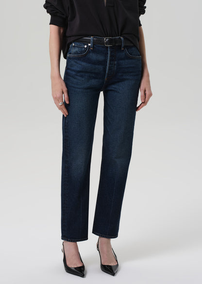 Person wearing a black sweater and dark blue jeans on a grey background