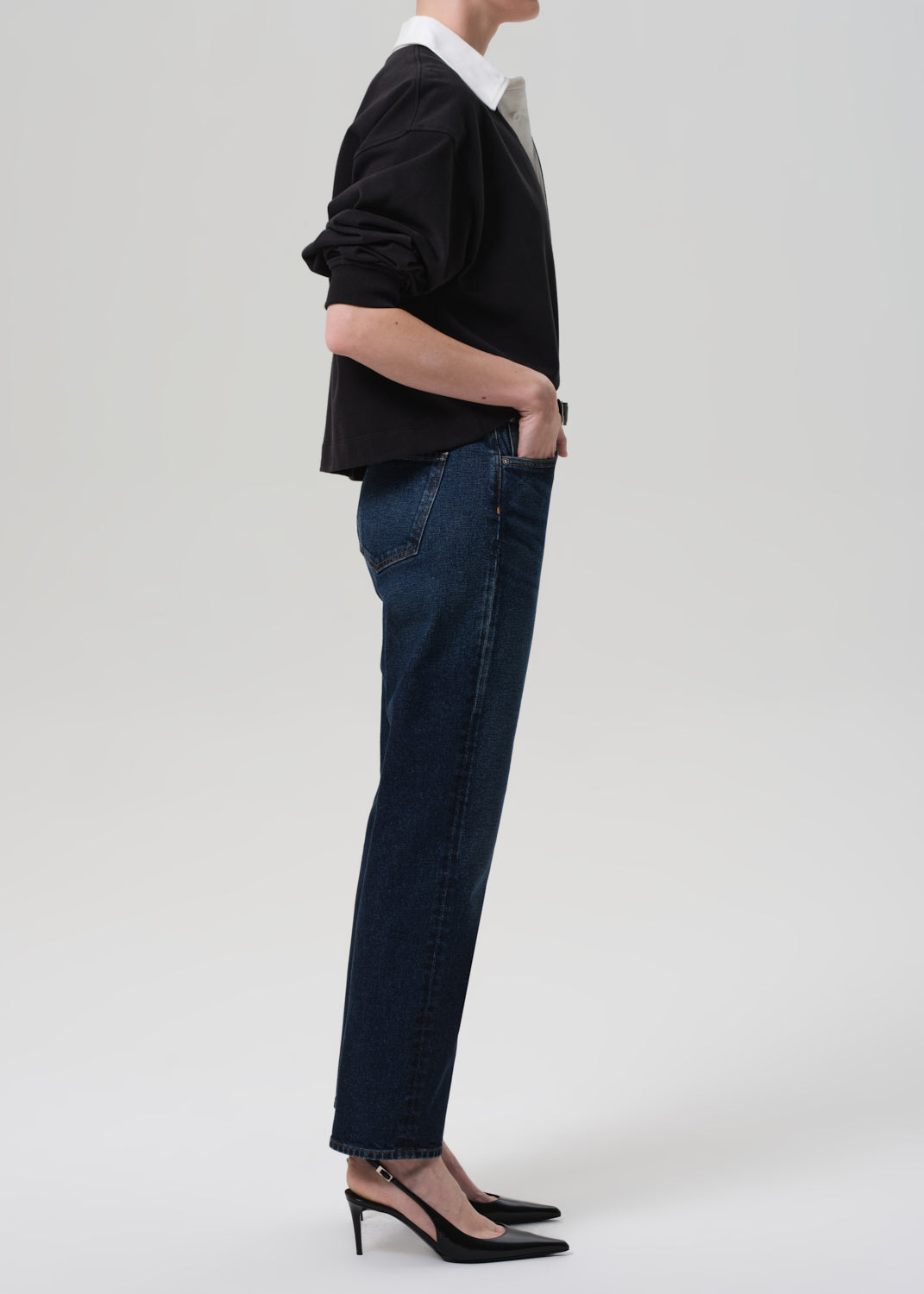 Person wearing a black sweater and dark blue jeans on a grey background
