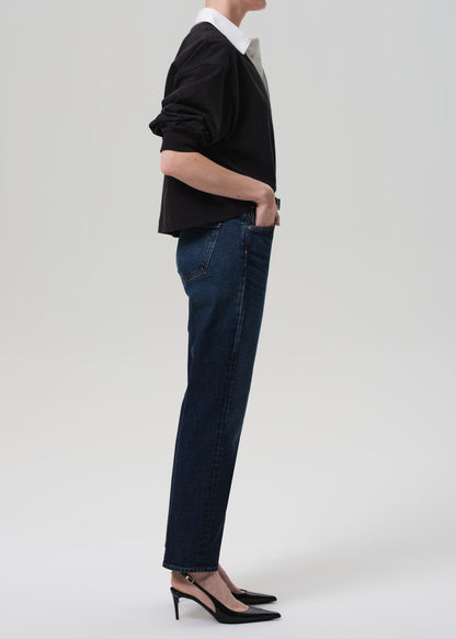 Person wearing a black sweater and dark blue jeans on a grey background