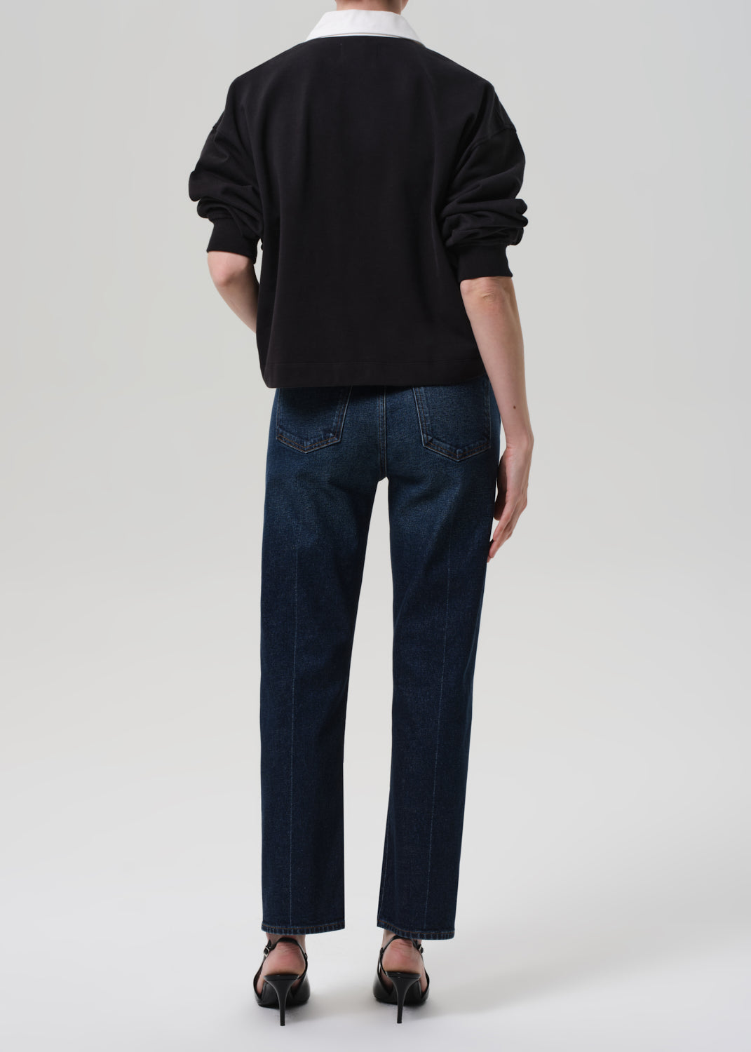 Person wearing a black sweater and dark blue jeans on a grey background