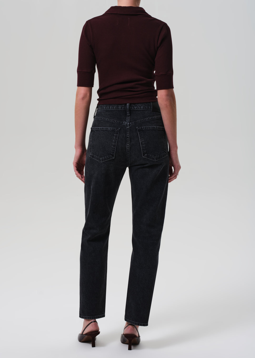 Person wearing a brown polo shirt and black jeans on a white background