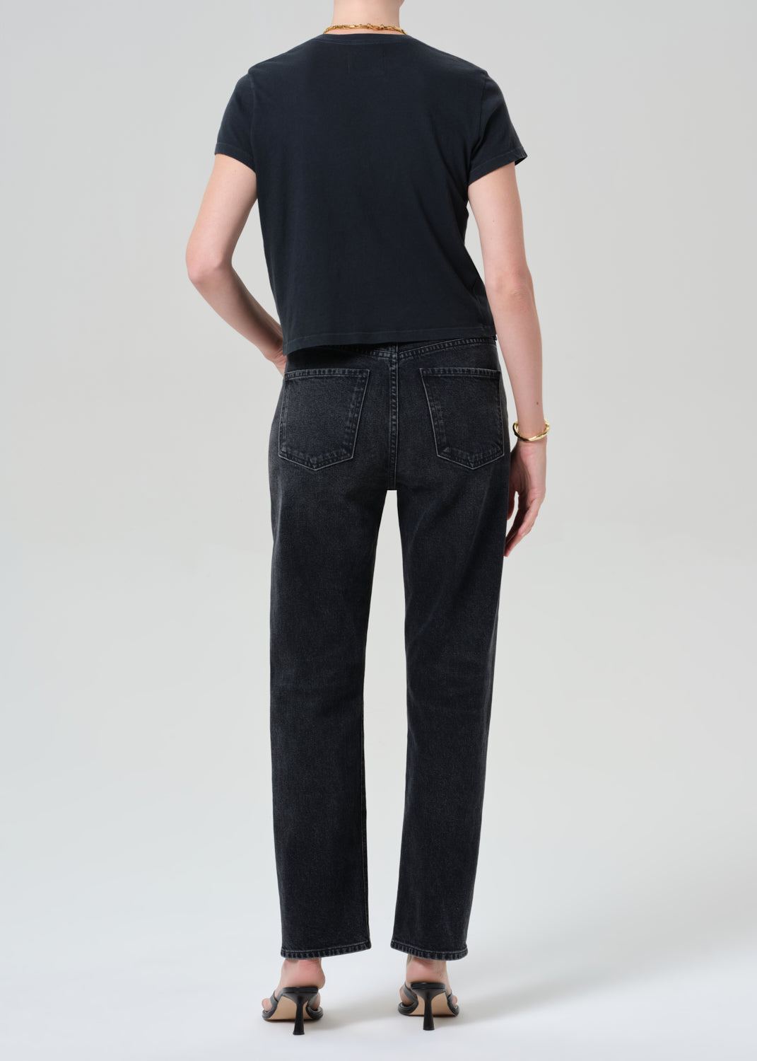 Person wearing a black t-shirt and black jeans on a grey background