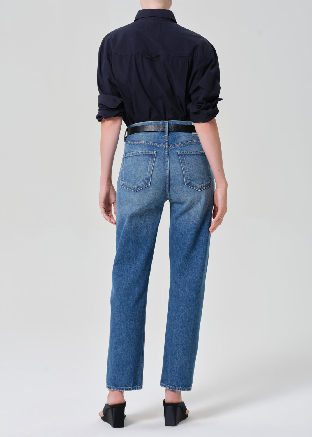 Person wearing blue jeans and a navy shirt on a grey background